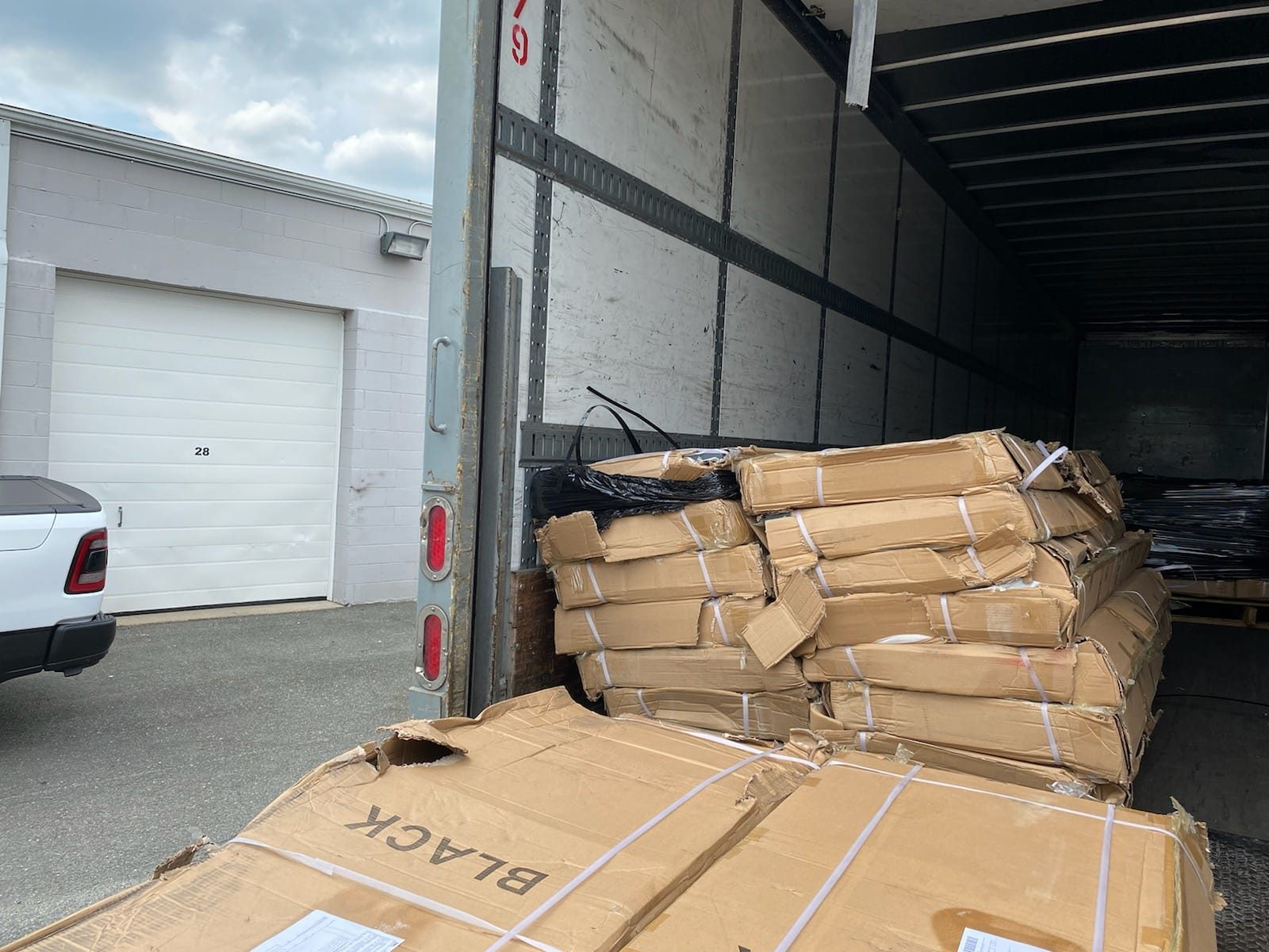 Damaged locker shipment in the back of a freight truck: stacked cardboard cartons with torn corners and split seams at a US warehouse loading bay