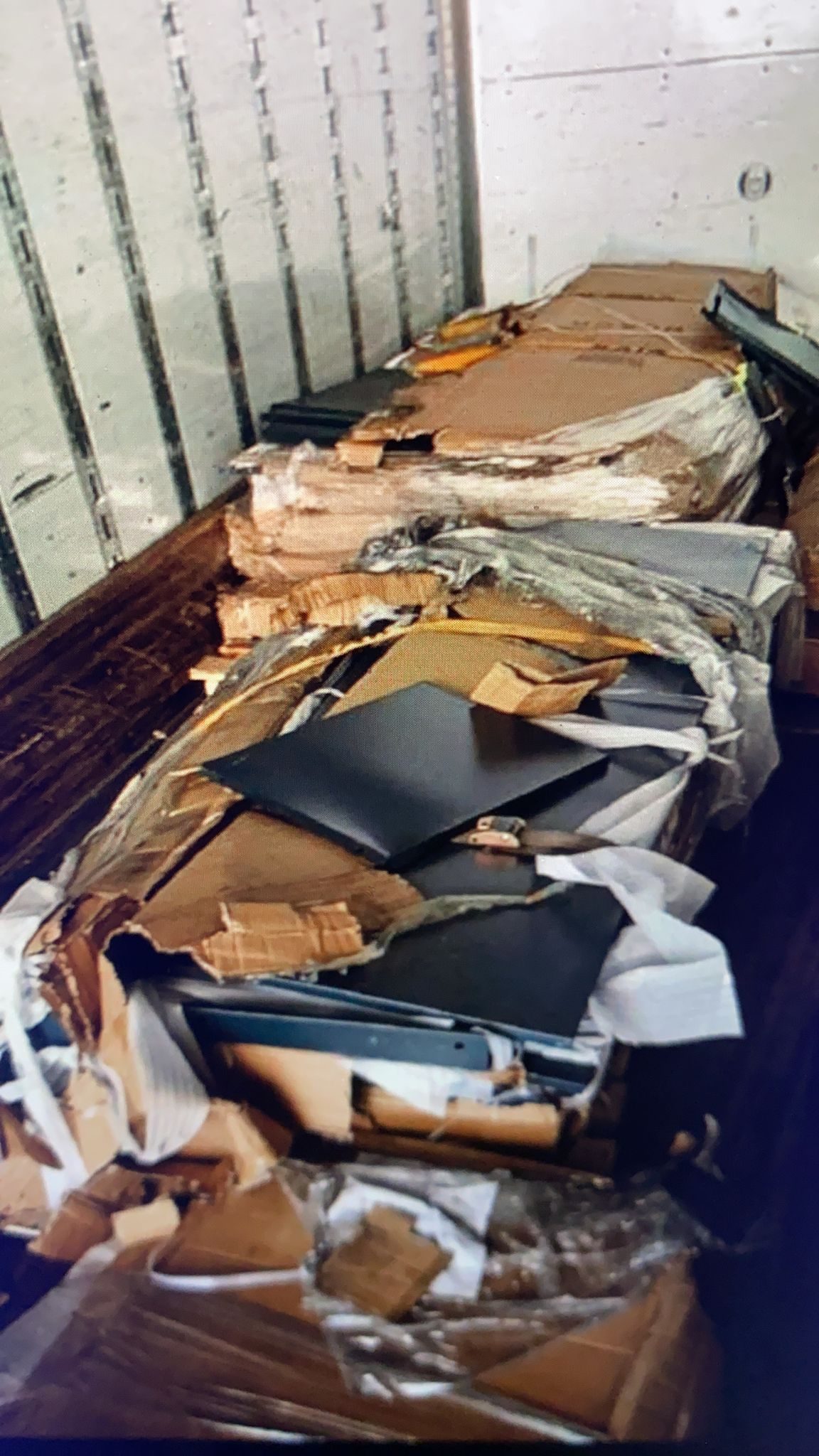 Inside a freight truck, black metal locker panels exposed through ripped cardboard packaging after international shipping