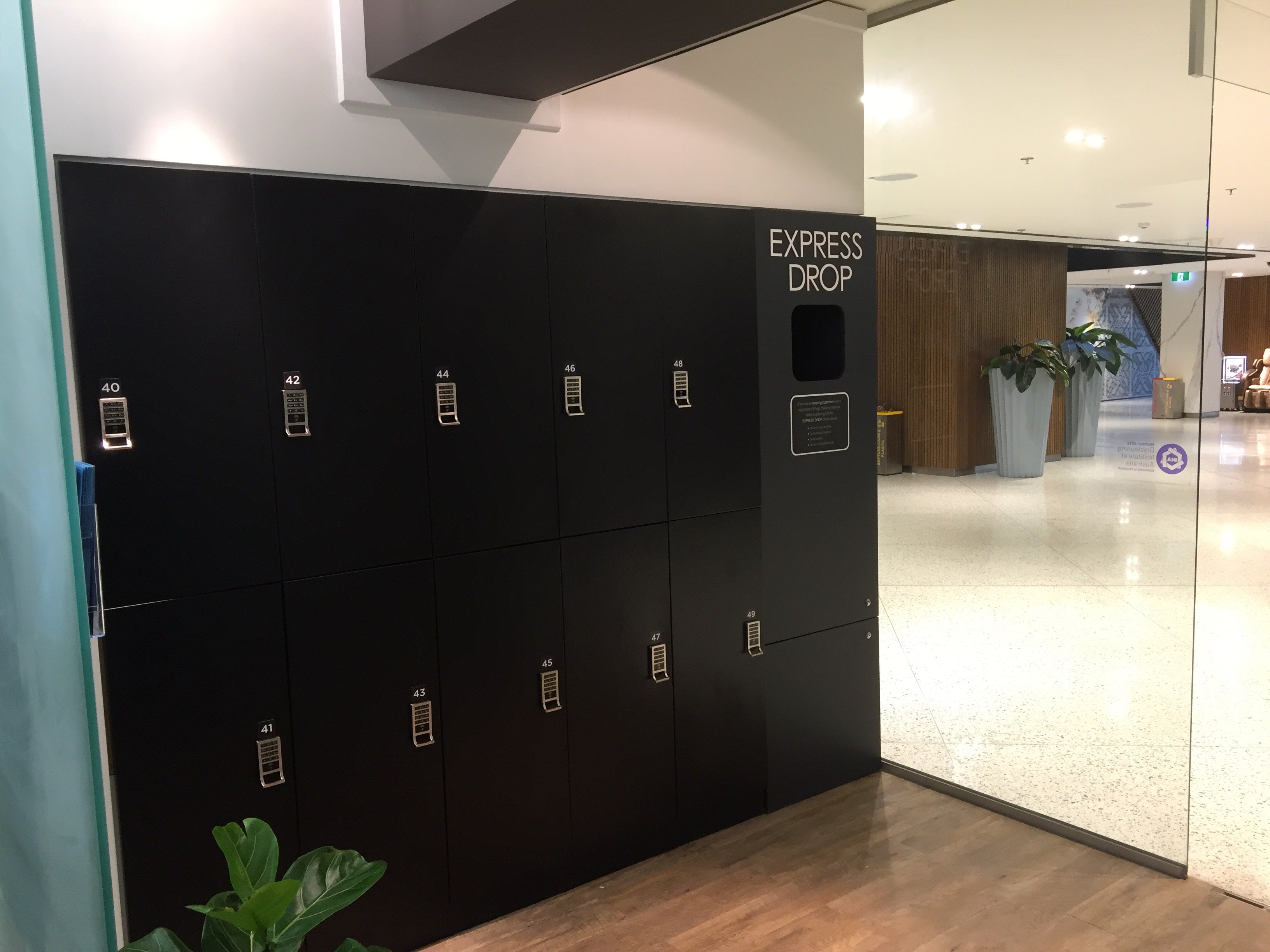 Bank of black Express Drop laundry lockers installed in a polished commercial office building lobby with a glass partition