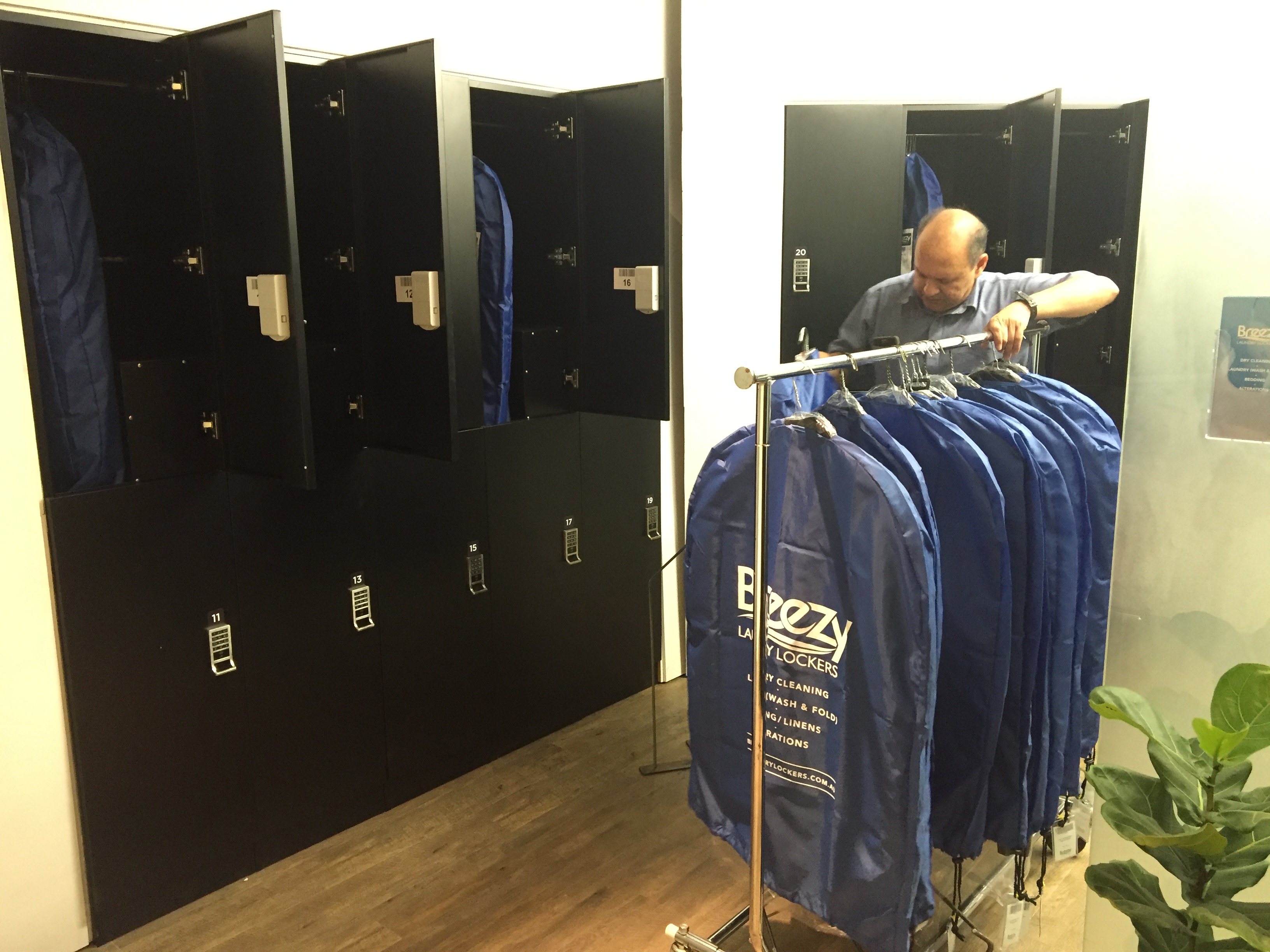 The owner restocking finished orders in branded blue garment bags on a rolling rack inside the operating store